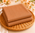 Folded camel beige lightweight scarf with fine textured weave, on wicker basket